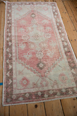 Angled view of a distressed Oushak runner with a faded red diamond medallion and sea foam green spandrels.