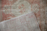 Corner of a distressed Oushak rug folded back to show the hand-knotted foundation.