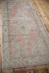 Angled view down the length of a vintage Oushak runner in soft blush and pale green tones.