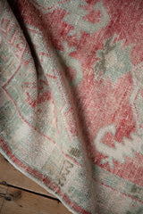 Close-up of a distressed vintage Oushak's soft, low pile in raspberry and celadon.