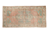 Vintage distressed Oushak rug runner with a faded pink, mint green, and ivory floral medallion design.