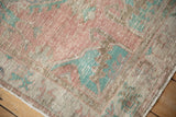 Textured corner of a vintage Turkish rug showing faded pink and pale turquoise spandrel details.