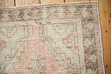 Corner detail of distressed Oushak rug, showing worn pile, faded rose, and seafoam green.