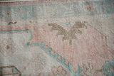 Distressed pile of vintage Oushak rug with dusty rose and pale turquoise floral motifs.
