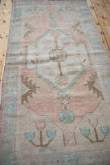 Distressed vintage Oushak runner with pale turquoise floral motifs on dusty rose.