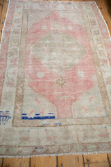 Angled view of a distressed Oushak rug showing its cobalt blue accent and faded pink medallion.