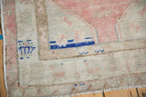 Corner detail of a distressed Oushak rug showing cobalt blue accents on the ivory and pink border.
