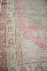 Angled view of the distressed Oushak's worn texture, showing faded pink and sand motifs.