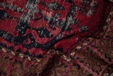 A folded view showing the distressed texture of a vintage rug with red, navy, and brown patterns.