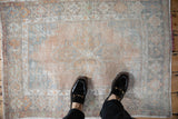 Small vintage distressed Oushak rug with a faded palette of orange and silver, shown for scale.