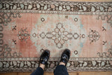 Vintage distressed Oushak runner with feet showing faded cantaloupe, sandalwood, and vine motifs.