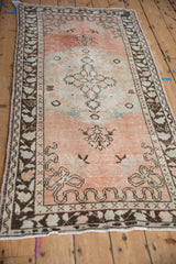 Corner of distressed Oushak rug with faded cantaloupe field, chocolate border, and cloud-band.