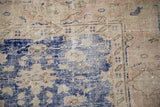 Distressed Oushak carpet close-up reveals worn pile, visible foundation, and vibrant cobalt blue motifs.