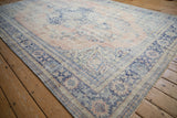 Vintage distressed Oushak corner: worn rose field, faded blue border, stylized floral motifs.