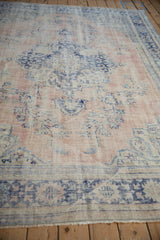 Distressed vintage Oushak carpet displaying worn rose and denim blue floral motifs.