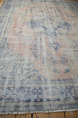 Vintage distressed Oushak carpet's worn fringe and faded rose and blue pile.