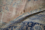 Distressed hand-knotted Oushak rug pile showing visible wear, rose, beige, and blue tones.