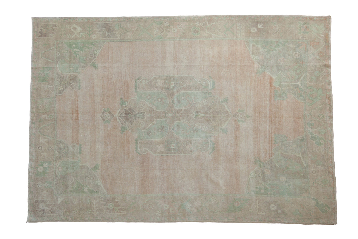 Distressed vintage Oushak carpet with a soft blush field, large mint green medallion, and corner spandrels.