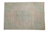 Distressed vintage Oushak carpet with a soft blush field, large mint green medallion, and corner spandrels.