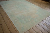 Angled view of a distressed Oushak carpet showing its soft, low pile and abrashed field in muted tones.