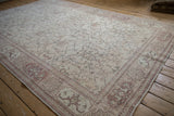 Angled view of a distressed Oushak rug, showing the faded floral field and dusty red geometric border.
