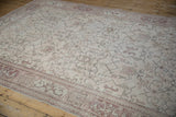 Angled view of a distressed Oushak carpet's faded geometric vines and floral blossoms.