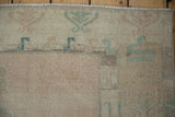 Heavy abrash and color variation on the corner of a distressed Oushak rug with soft rose and teal motifs.