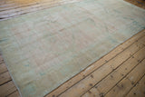 Angled perspective of a distressed Oushak runner with heavy abrash in pale rose and sand.
