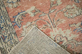 Lifted corner of a vintage distressed Oushak rug, revealing its faded dusty rose pile and neutral woven foundation.