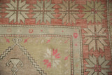 Distressed Oushak rug corner with pale brick red and sage green starbursts and florals.
