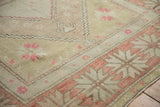 Distressed vintage Oushak rug's starburst border and pale brick red pinwheel floral fills.