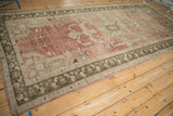 Distressed vintage Oushak rug corner, showing faded red field with abrash, and bronze geometric border.