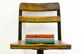 Antique school chair's wooden seat and iron frame, with stacked orange and blue books.