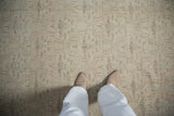 Feet on distressed Oushak rug, showing faded pink, green, and brown scalloped trellis pattern.