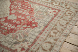Worn, low pile texture over the corner spandrel's cherry red and ivory stylized motifs.