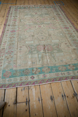 Distressed Soumac design rug corner with dusty rose wave and turquoise gul floral borders.