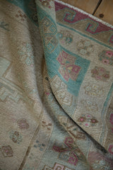 Folded vintage distressed Soumac carpet displaying geometric patterns in ivory, turquoise, and rose.