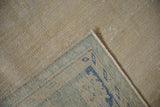 Folded corner of distressed Oushak carpet revealing textured foundation and patterned blue border.