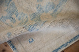 Distressed Oushak rug corner, showing soft wool pile and intact blue side cord selvage.