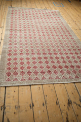 Vintage distressed Oushak rug showcasing worn diamond pattern in dusty raspberry and beige.