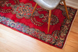 Vintage Persian Kerman rug corner, rich red field, detailed blue and red paisley border.