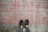 Distressed vintage Sparta carpet showing faded red and blue floral motifs, with visible foundation.
