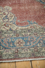 Dusty burgundy red distressed field and worn pile, with sky blue and ivory scrolling floral border.