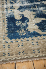Distressed vintage Oushak rug corner: cobalt blue and beige pattern, exposed foundation, bound edge.