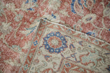 Distressed Sparta rug showing faded brick red floral motifs, worn pile, and machine-bound edge.