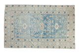 Distressed vintage Oushak rug: powder blue field, sand borders, geometric motifs, and starbursts.