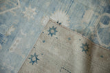 Distressed vintage Oushak rug's faded pile and beige foundation with blue star motifs.