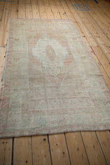 Angled view of a vintage Turkish Oushak rug showcasing its faded pastel medallion and distressed texture.
