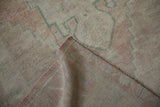 Folded corner of a distressed Oushak rug revealing the hand-knotted back and original side cord selvage.