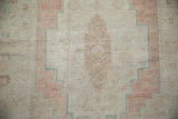 Low pile texture of a distressed Oushak rug showing a stepped medallion in blush, sand, and ocean green.